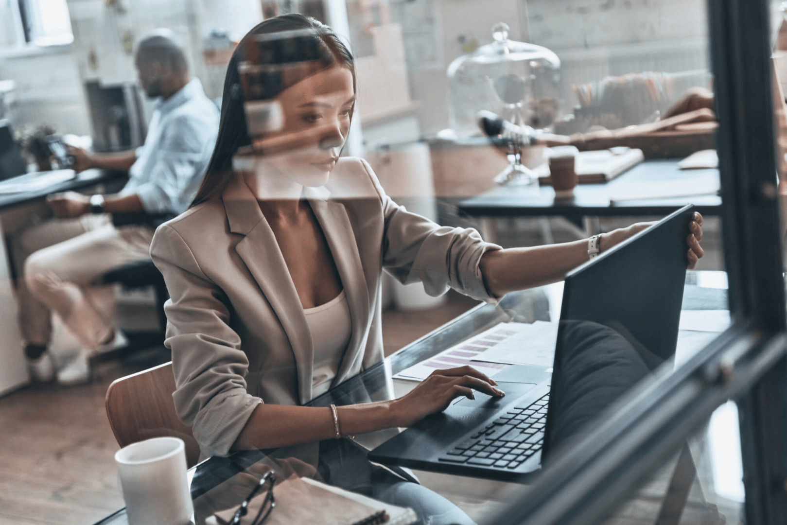 Escritório moderno e iluminado, com três pessoas trabalhando em seus respectivos laptops.