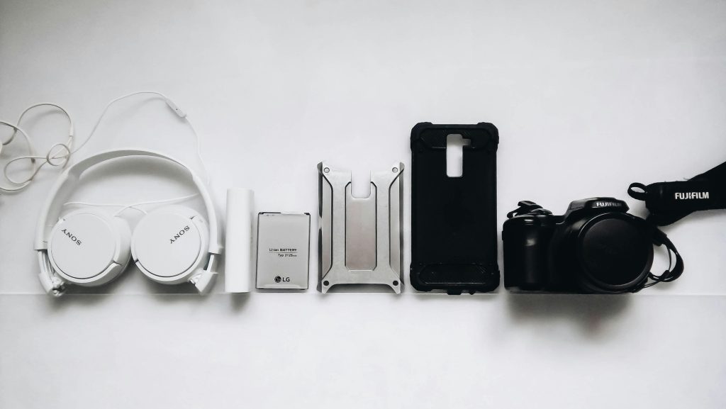 Fones de ouvido, power bank, capinha de celular, smartphone e câmera organizados sobre fundo branco.
