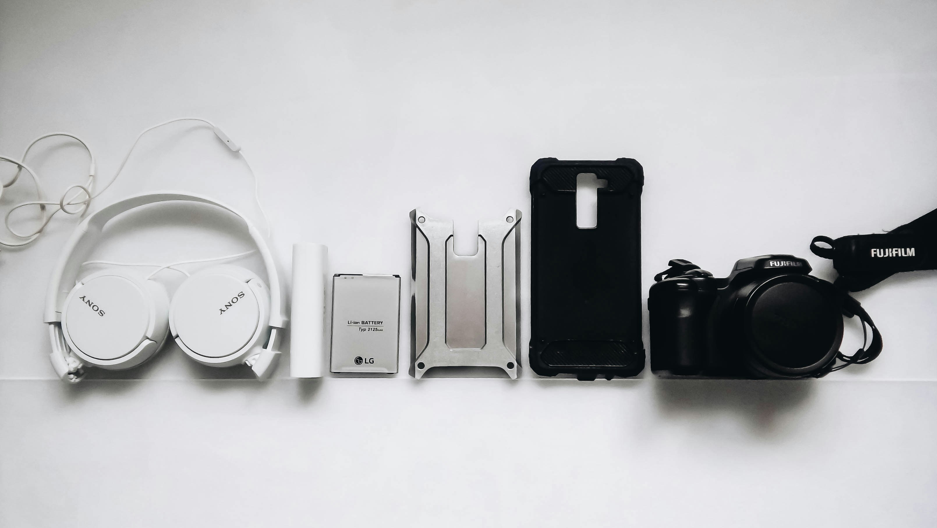 Fones de ouvido, power bank, capinha de celular, smartphone e câmera organizados sobre fundo branco.