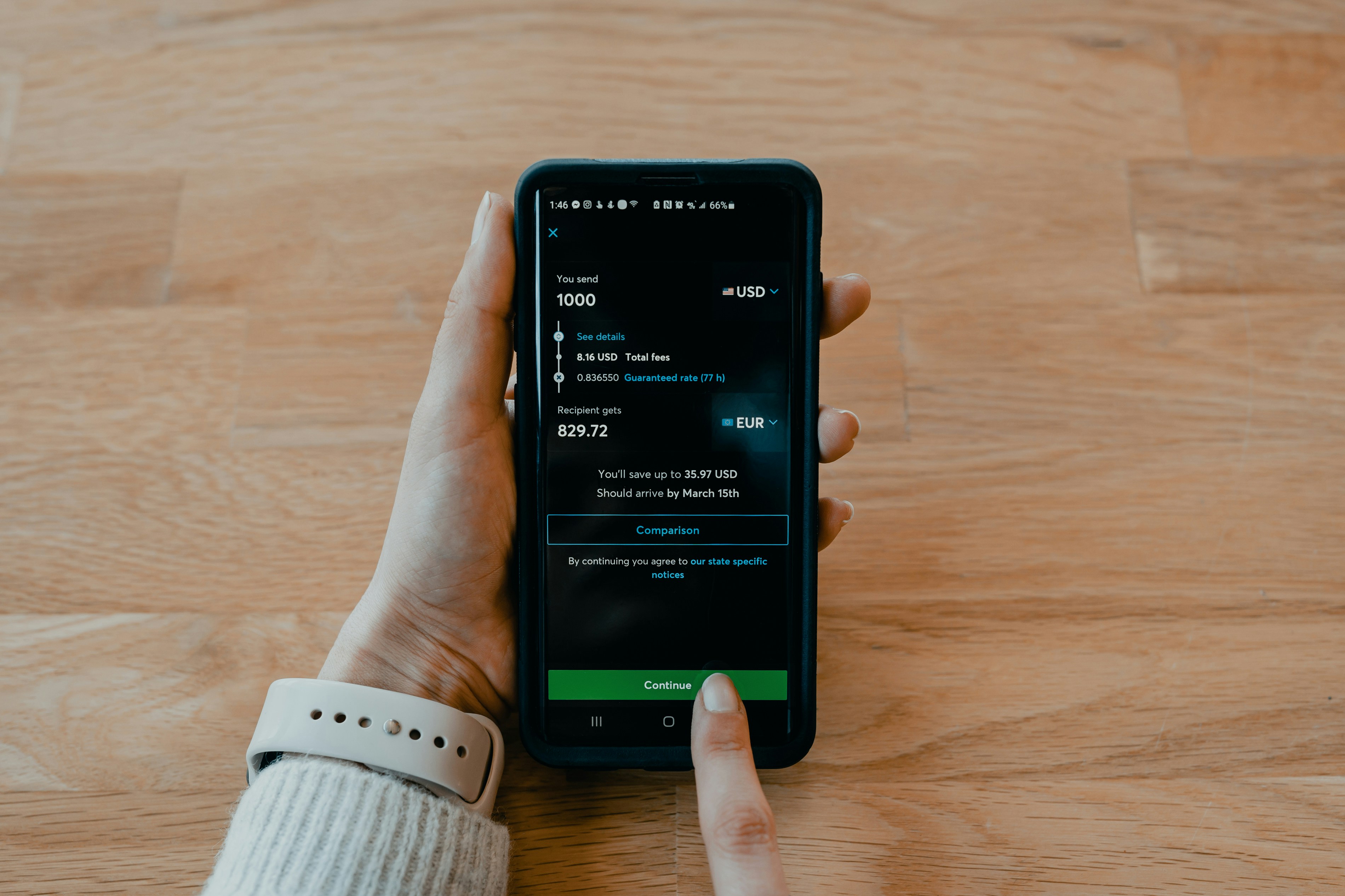 A imagem mostra uma mão segurando um smartphone com o aplicativo de um banco, indicando uma transferência. Nela será enviado 1.000 dólares e quem vai receber o valor o recebe em euros, totalizando 829,72 euros. Essa imagem representa os meios de pagamentos usados em transações de varejo e comércio.